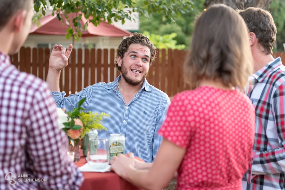 A man makes a point by using a hand gesture during party conversation at a backyard wedding celebration.