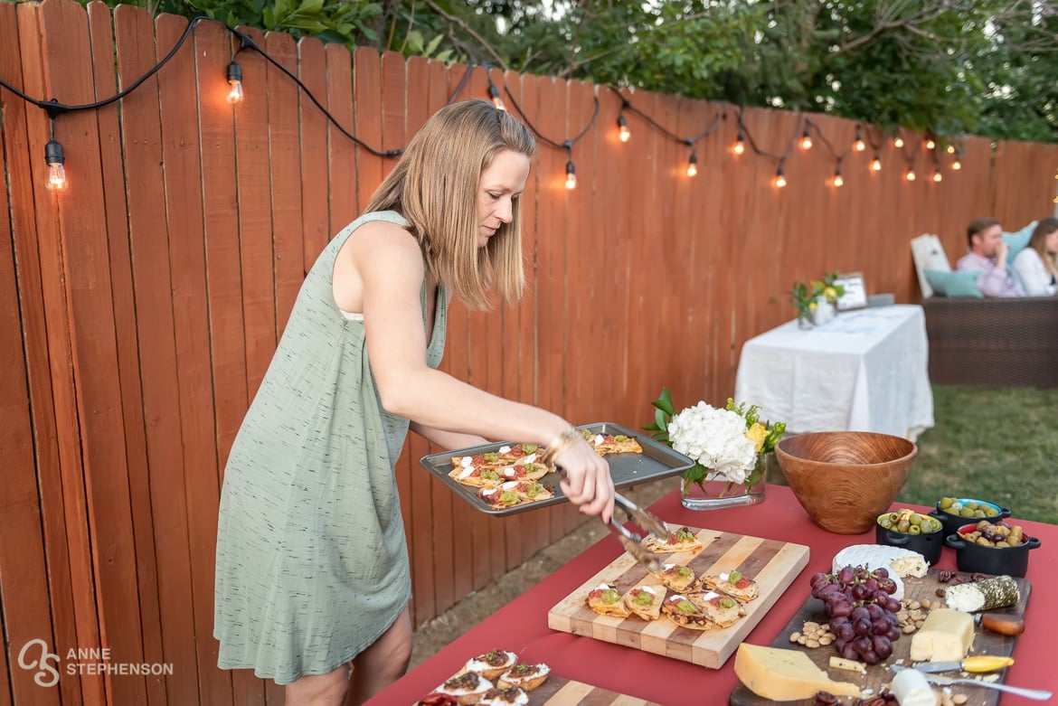 The hostess uses tongs to restock bites of food on the appetizer table.