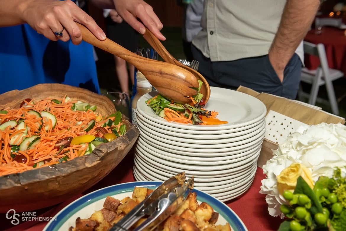 Close up of a woman serving a salad with tongs.