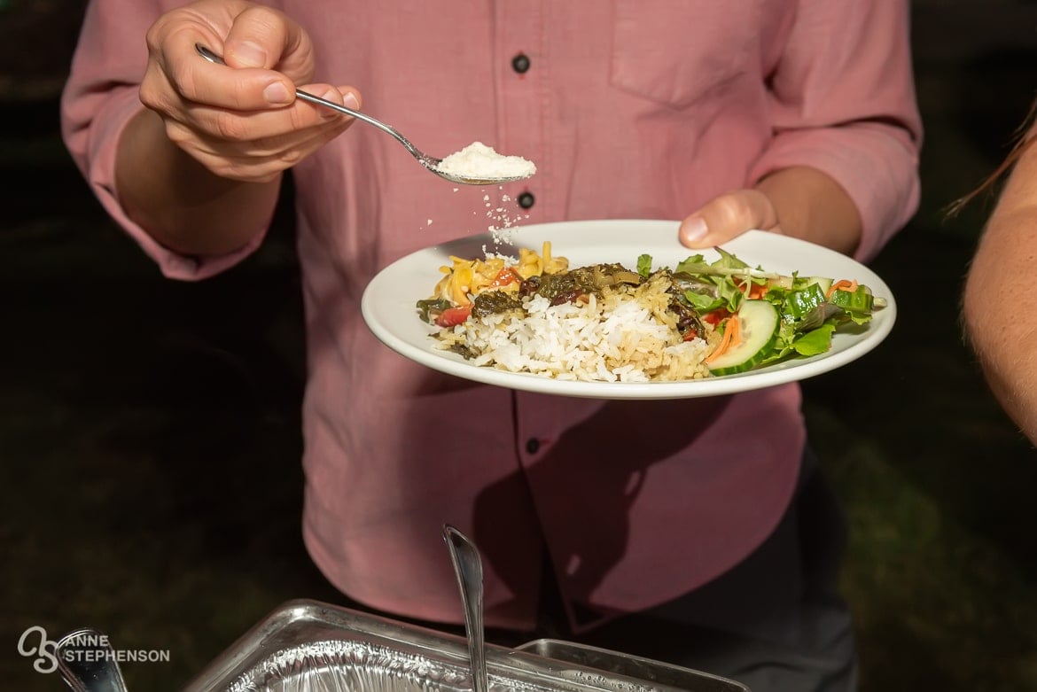 Close up of a man sprinkling parmesan cheese on his salad plate.