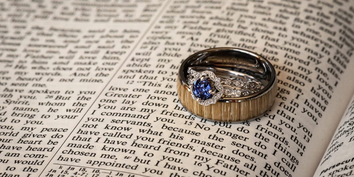 A wedding ring with a sapphire stone in the center on top of a favorite Bible passage