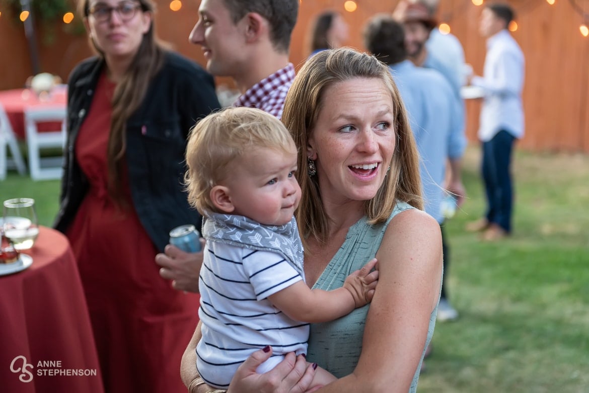 The hostess holds her infant son as she talks to guests at the party held for her recently married friend.