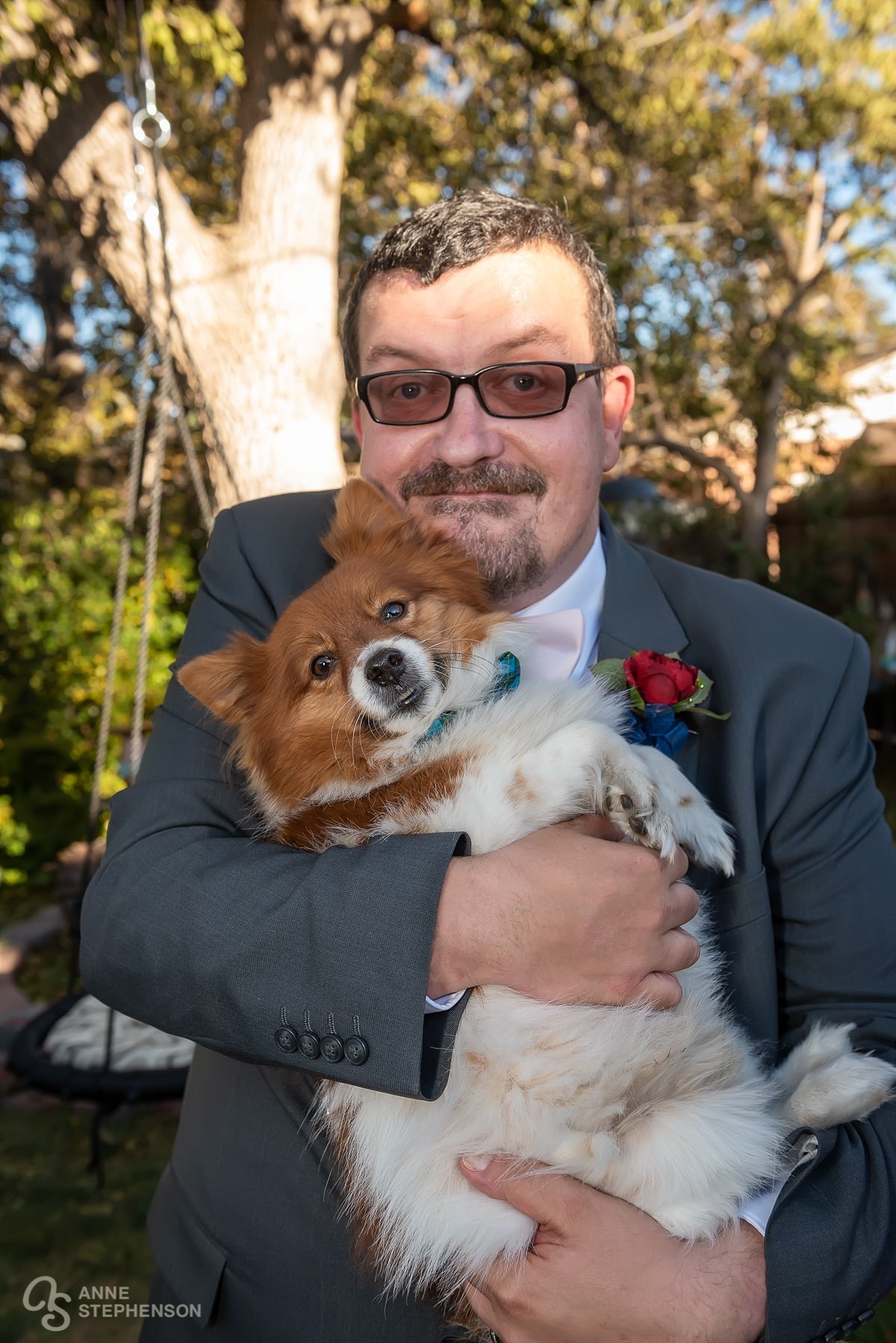 The groom holds a well groomed puppy wearing a bow tie.