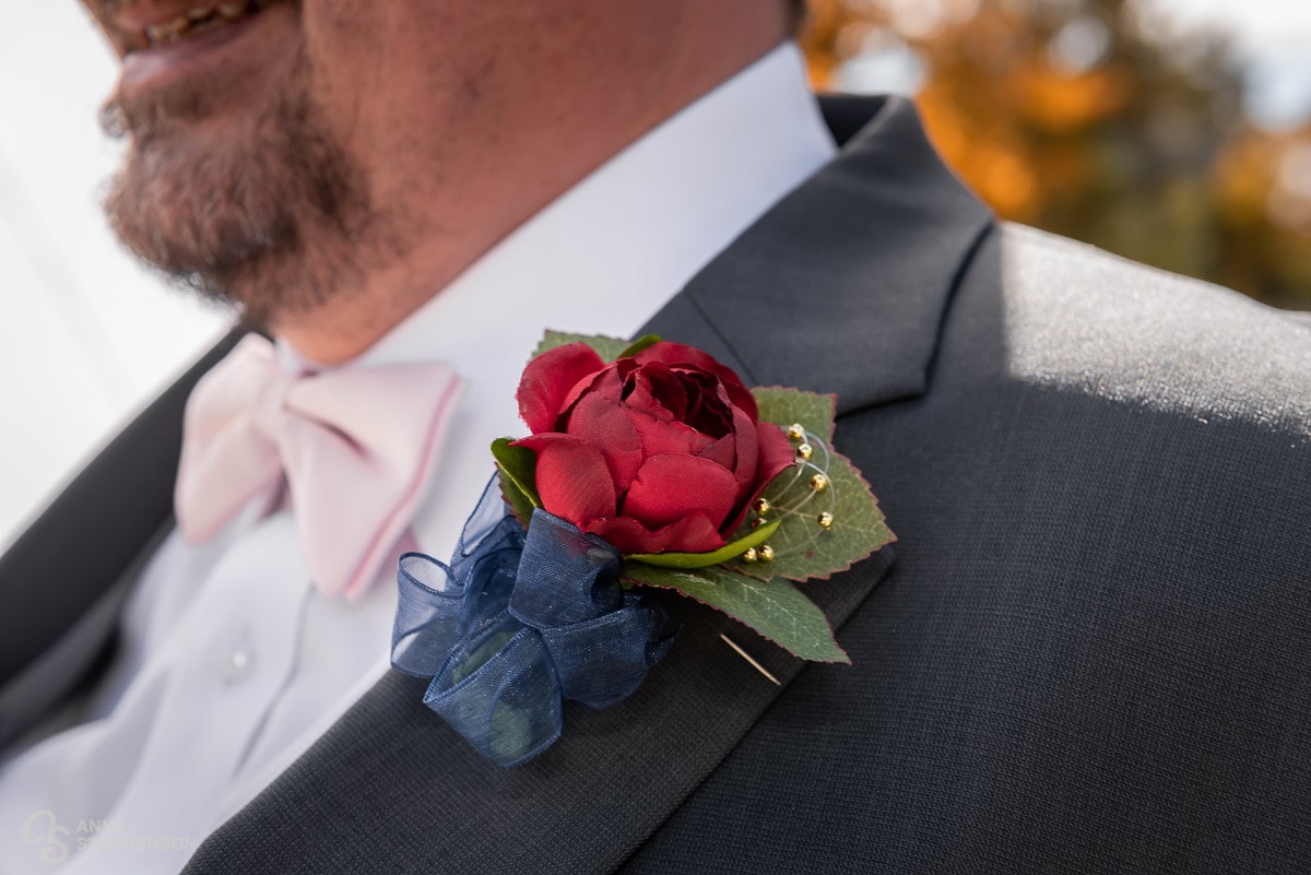 Close up of the groom's red rose boutonniere with navy ribbon, baby's breath and leaves.