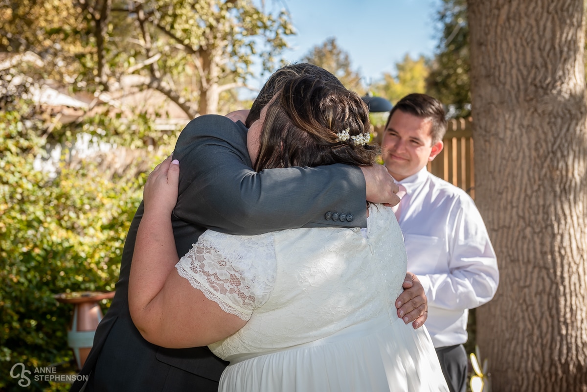 The groom hugs the bride after the exchange of the rings as the officiant looks on.