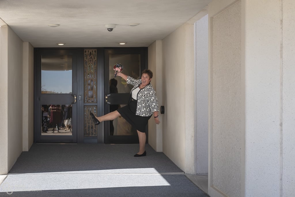 An excited mother of the bride kicks up one leg and poses in front of the temple entrance.