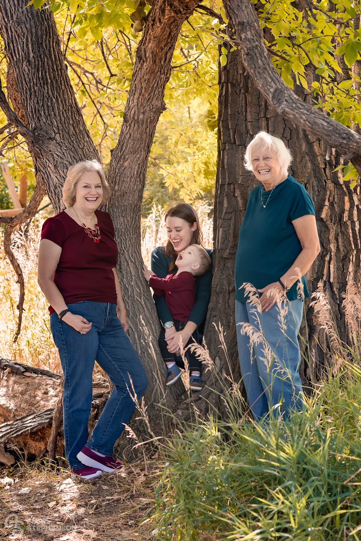 A multi-generational portrait of a grandmother, great-grandmother, mother and son stand between the trees at McKay Trail.