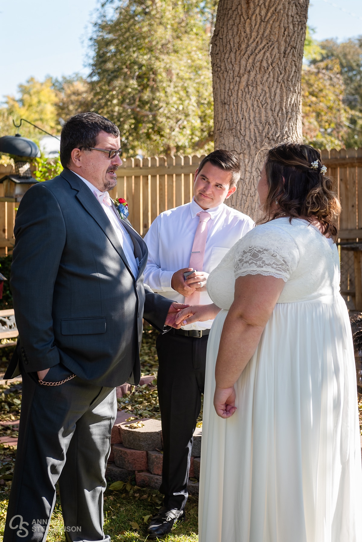 The bride and groom along with the officiant during the outdoor ring ceremony under large trees.