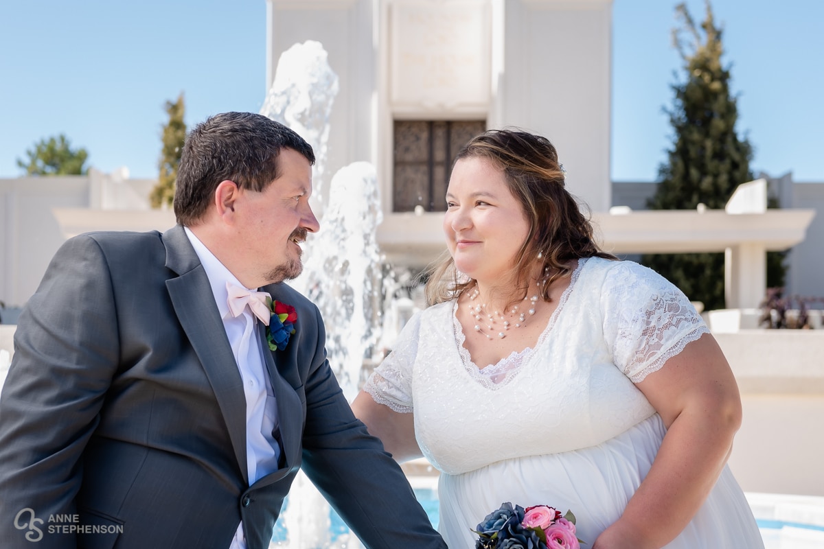 The bride and groom share conversation while seated on the edge of the fountain in front of the Denver LDS Temple.
