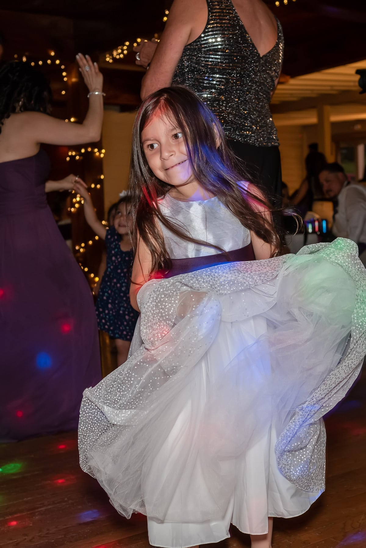 A young flower girl flounces her skirt and dances at a wedding reception.