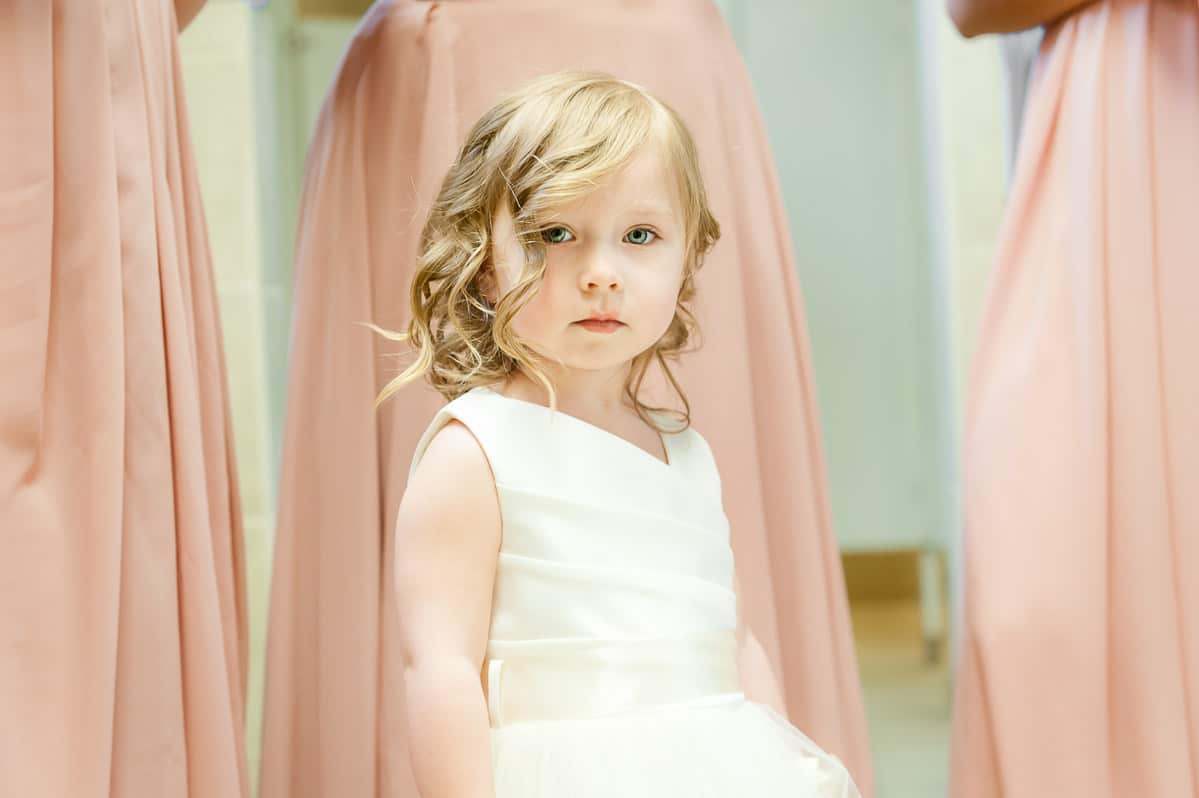 A flower girl stands in front of the bridesmaids and looks intently at the camera.