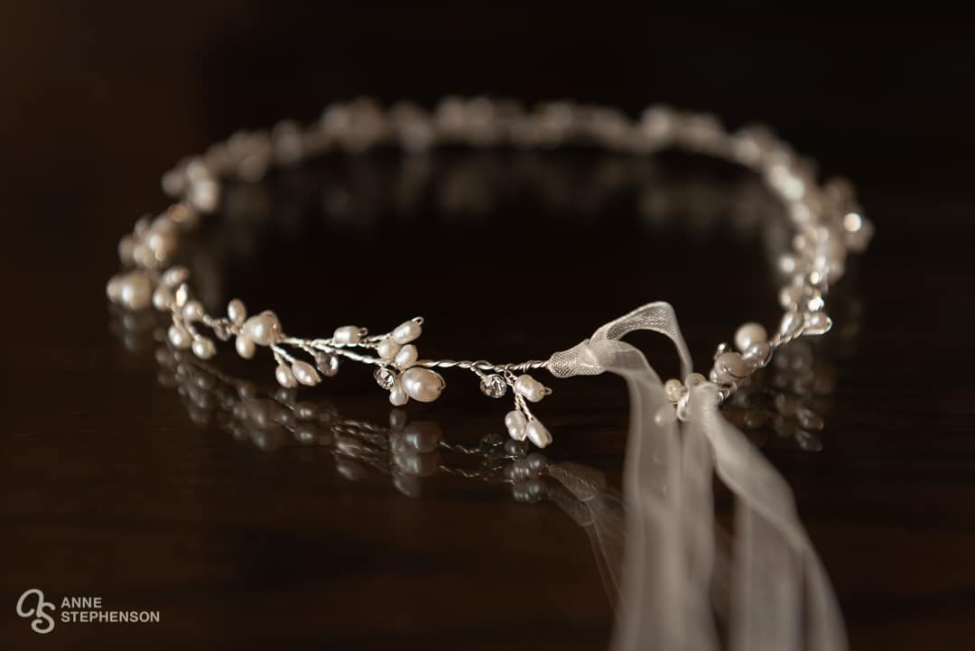 A delicate beaded bridal headpiece with pearls and ribbon on a wire frame.