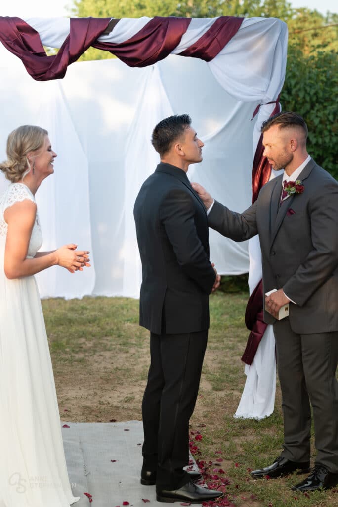 The best man primps the groom before the first kiss by straightening his tie.