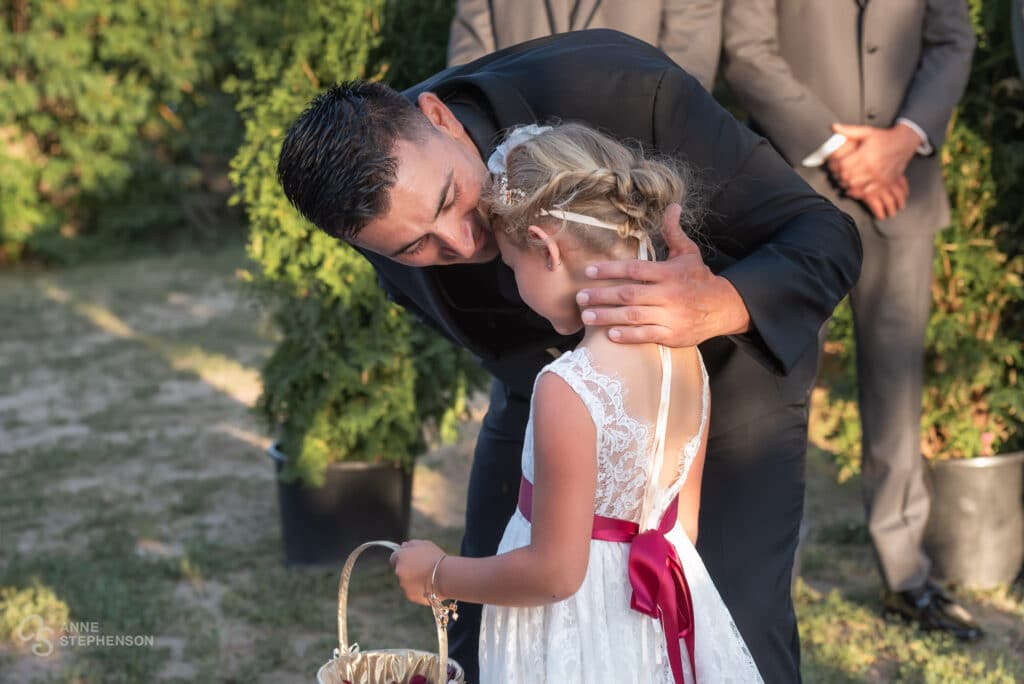 The groom kisses the forehead of his daughter after making her way down the aisle tossing rose petals.