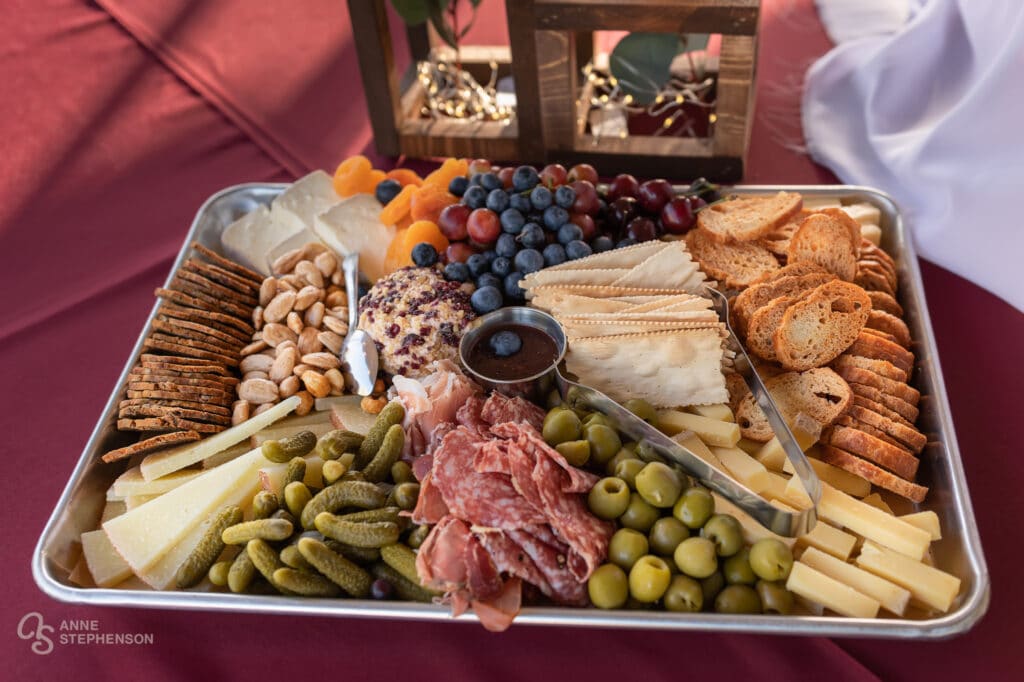 A charcuterie tray filled with crackers, cheese, nuts, olives, grapes and small pickles.
