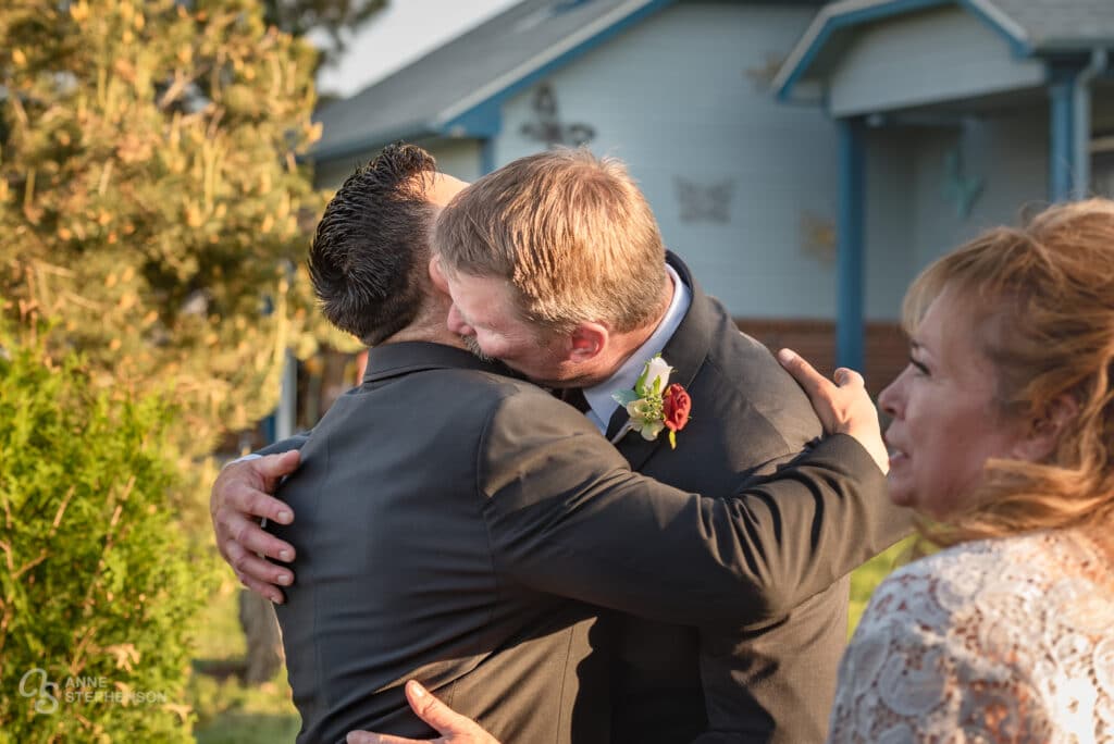The groom and his father embrace in a hug at the front of the aisle.
