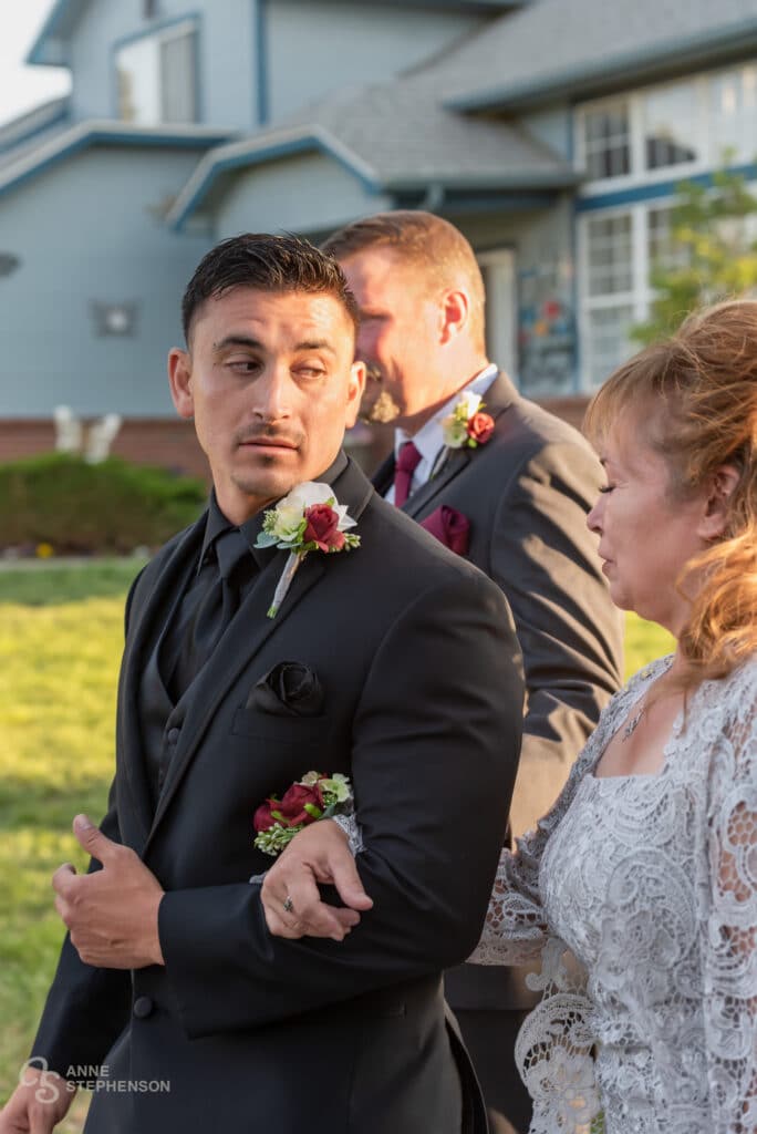 The groom reaches the front of the aisle and looks intensely with emotion at his mother.