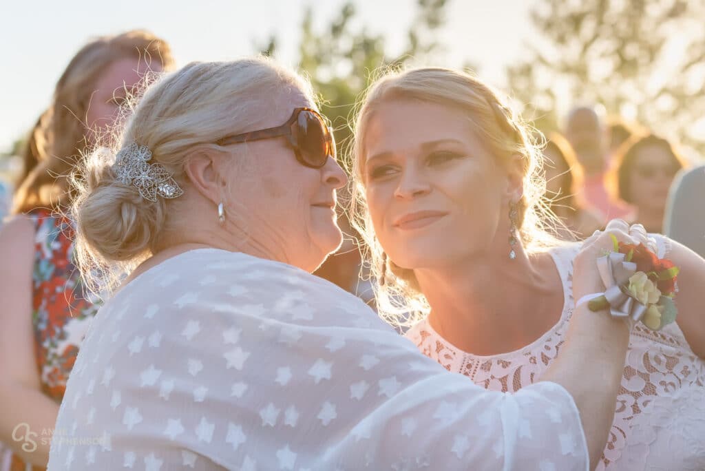 The mother of the bride embraces her daughter as the beautiful warm sunlight illuminate them from behind.