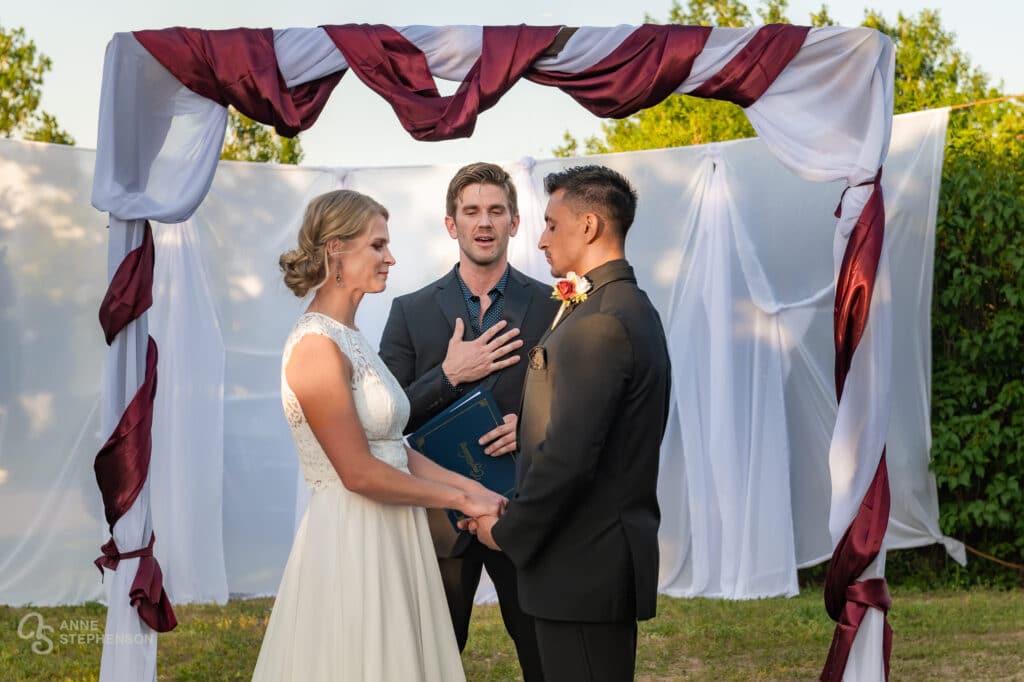 The officiant places his hand over his heart as the bride and groom hold hands during the ceremony.