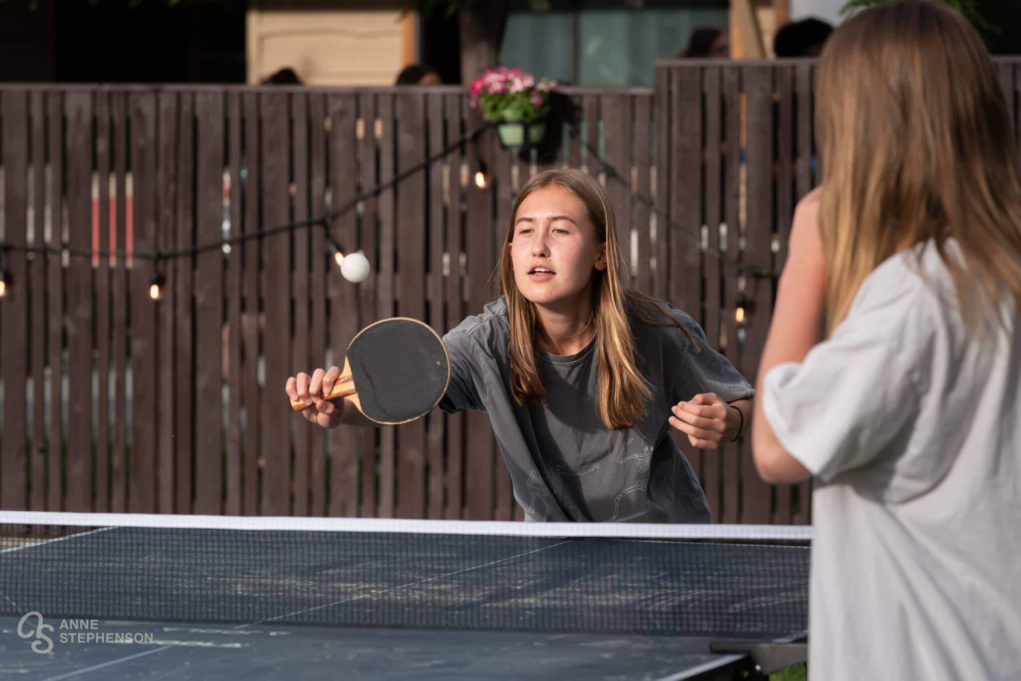 A young teen returns a ping pong ball during a lively outdoor game.