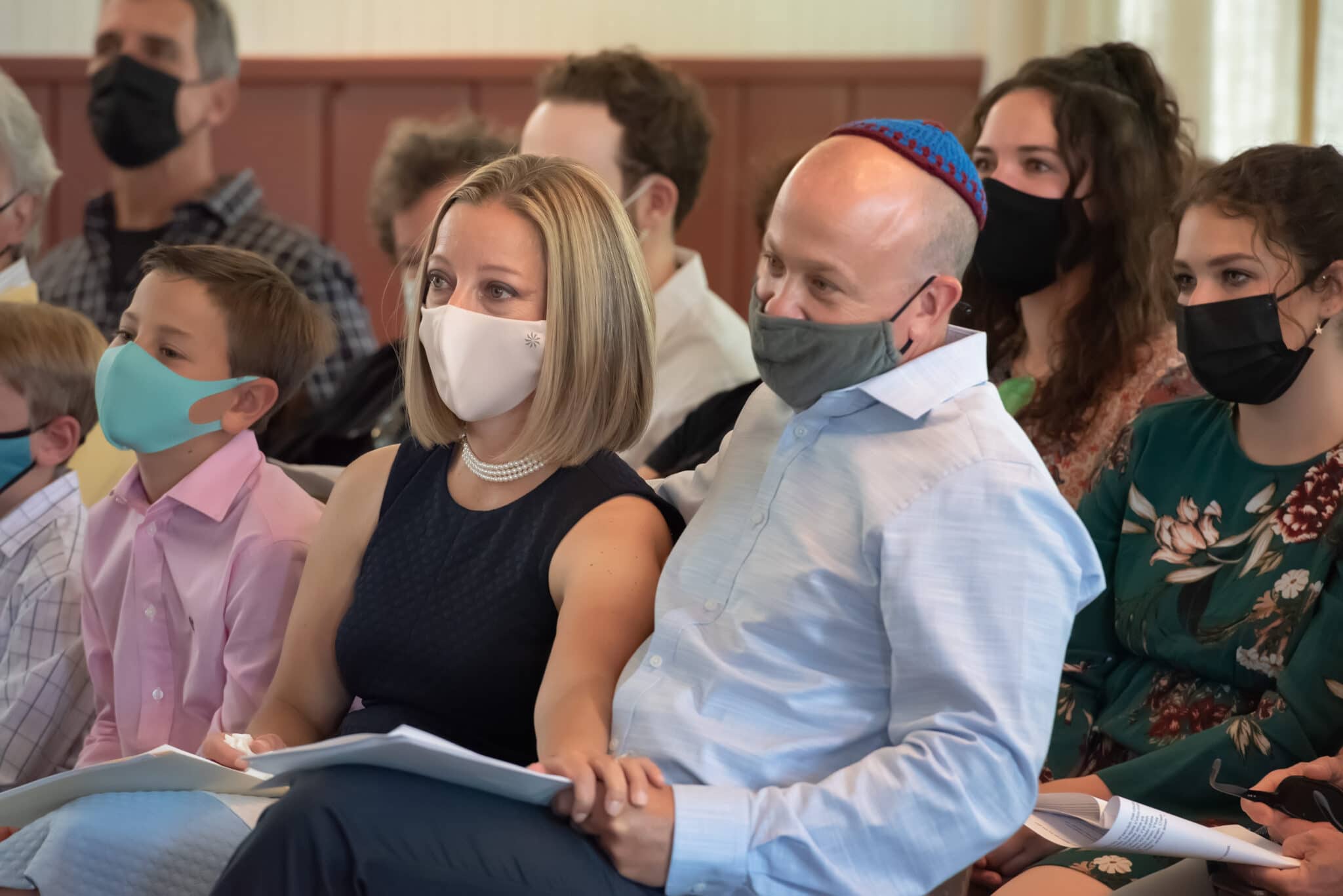 Proud parents wearing covid-19 masks watch their son lead the congregation during his mitzvah.