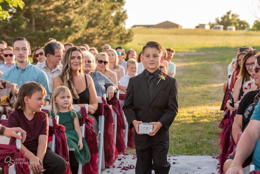 A young boy carries the rings up the wedding aisle in a box.