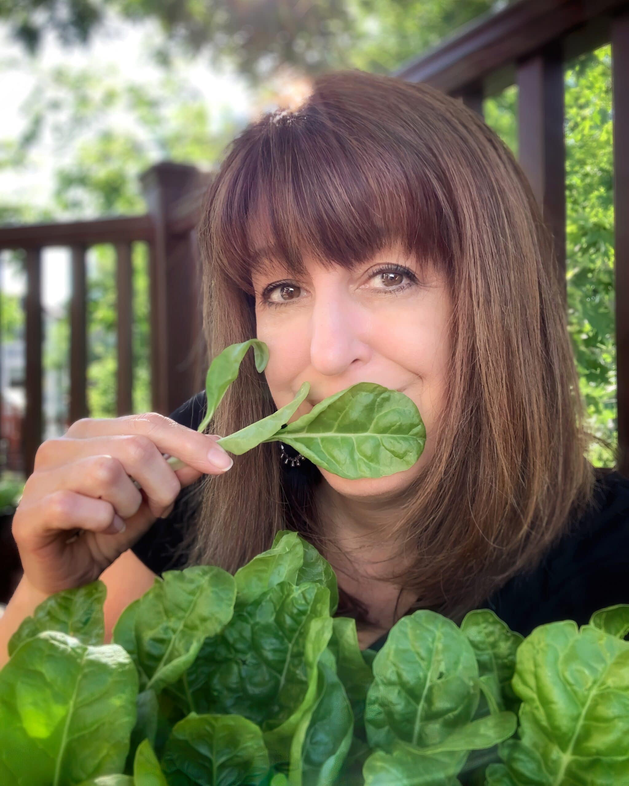 A photographer places a leaf of chard from her garden over her mouth.