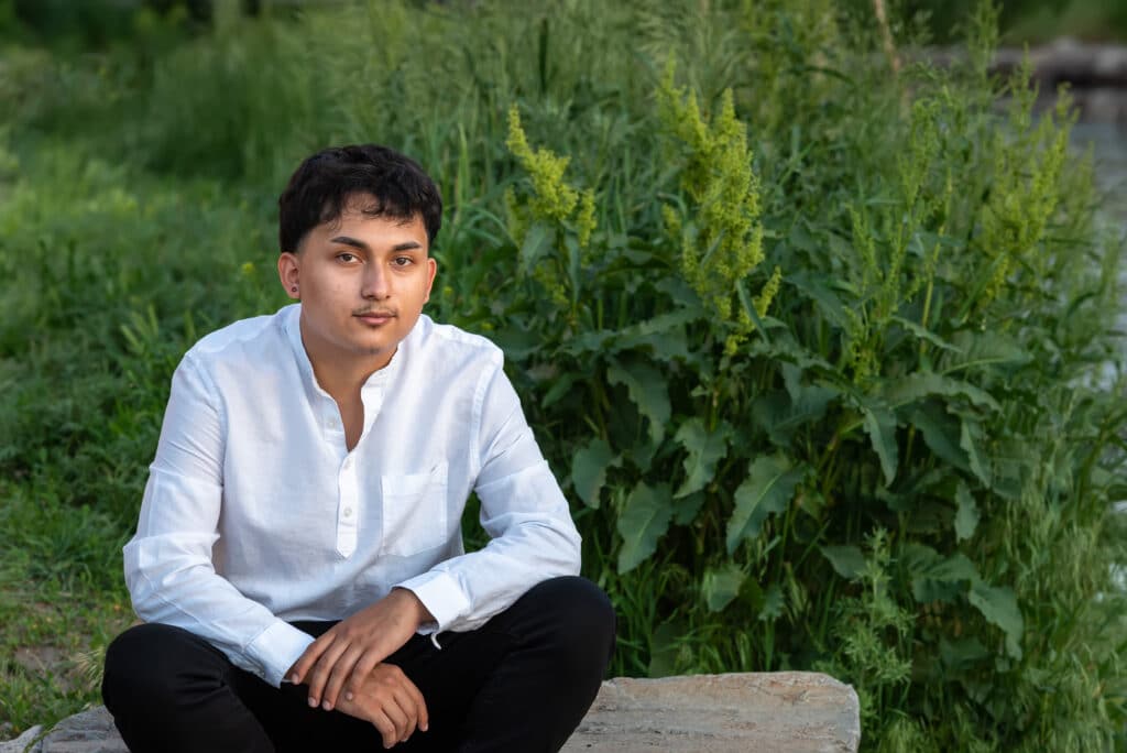 A young man sits on a stone bench surrounded by greenery during his senior photo session in downtown Denver.