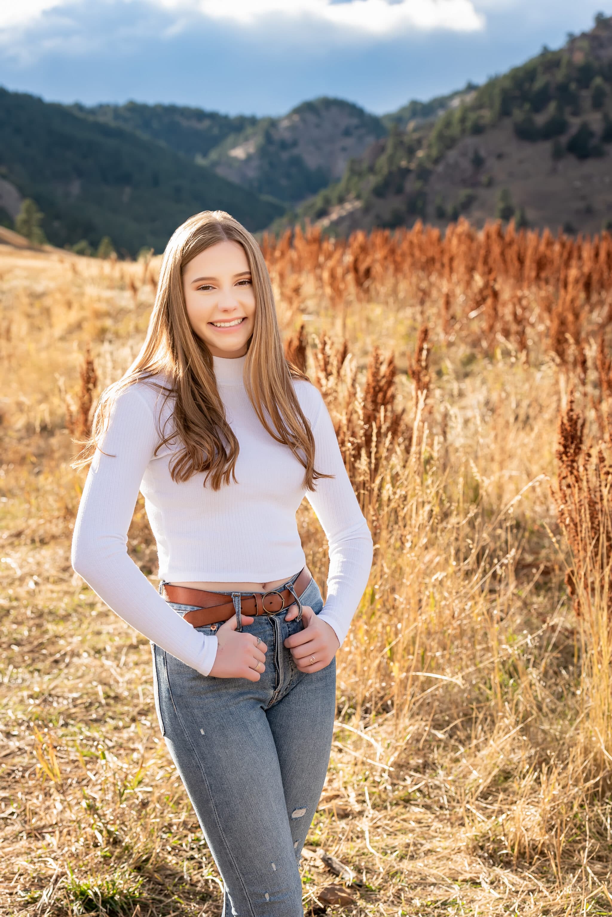 A young woman in a white turtleneck shirt, denim jeans and a belt at Chautauqua Park.