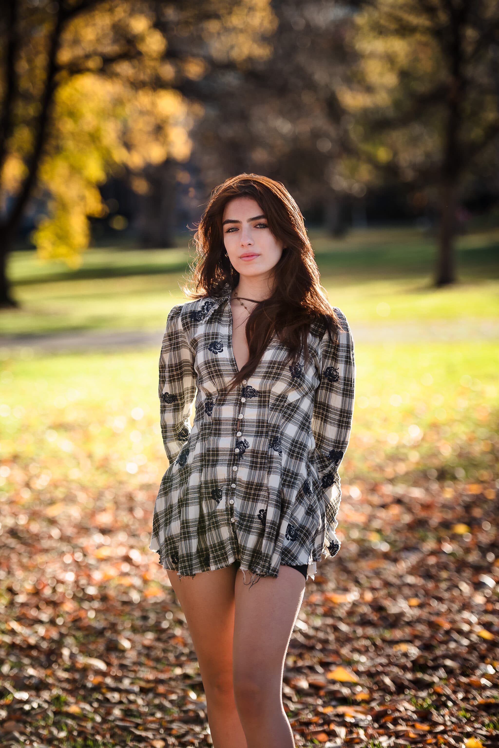 A young woman stands in a pile of leaves with the fall foliage surrounding her at City Park, Denver.