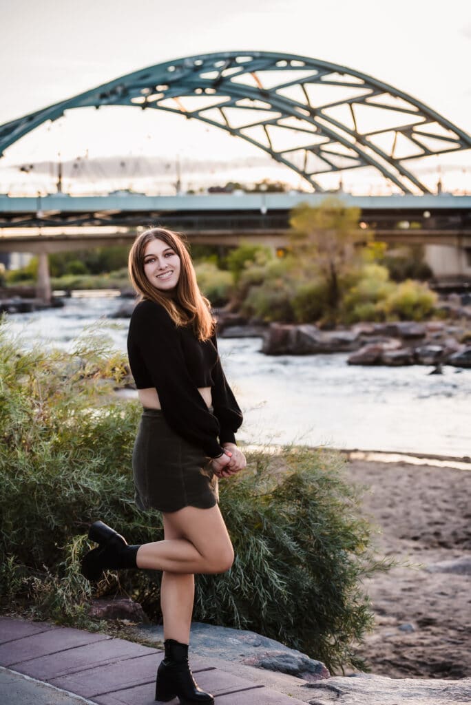 A young teen dressed in black kicks up her heels as the sun sets behind the bridge arching overhead in downtown Denver.