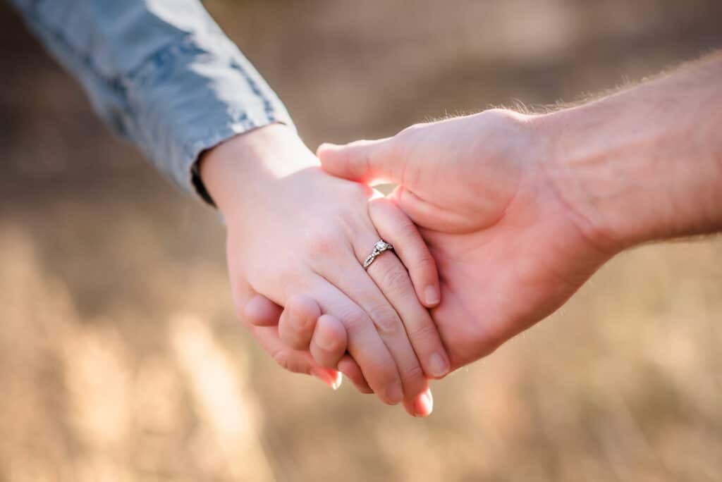 A close up of a woman wearing an engagement ring and a man holding hands.