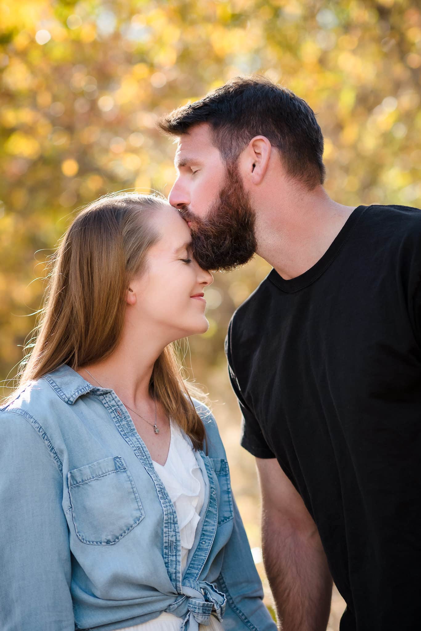 A man kisses his girlfriend on the forehead during their photo engagement session.