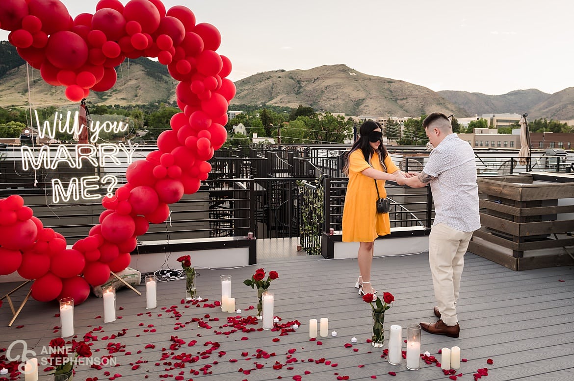A man leads his blindfolded girlfriend to a surprise romantic setting for an engagement proposal.