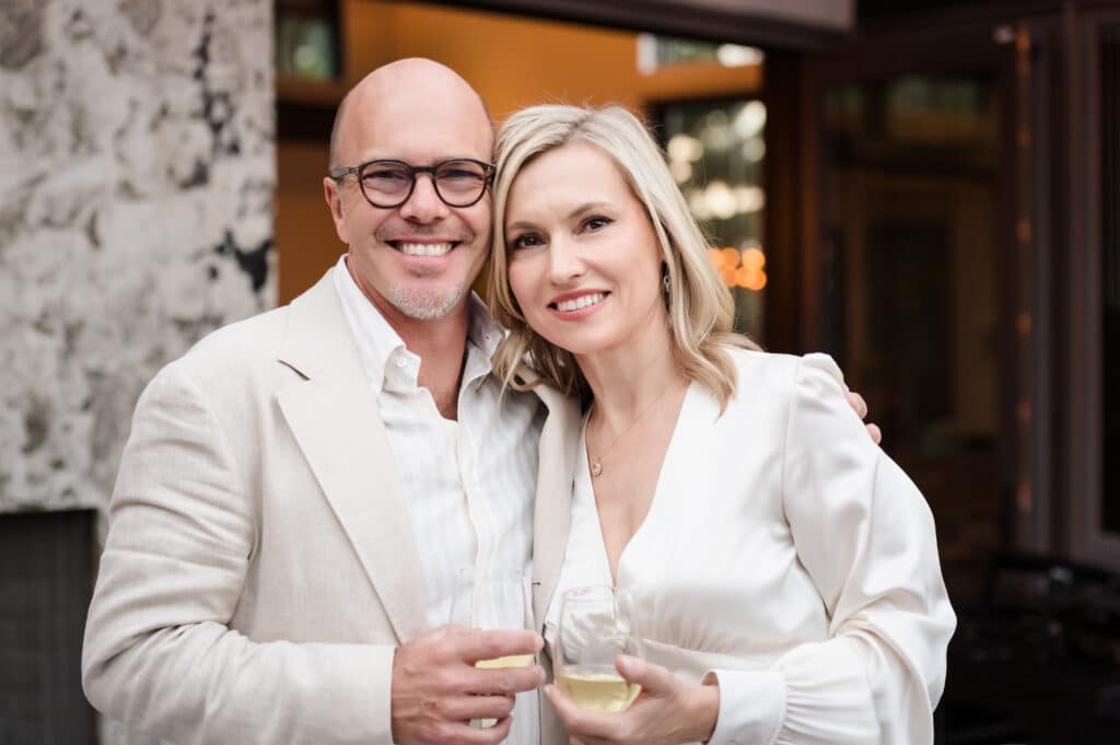 A couple's portrait of a man and his wife holding glasses of white wine at the 50th birthday party he planned for her.