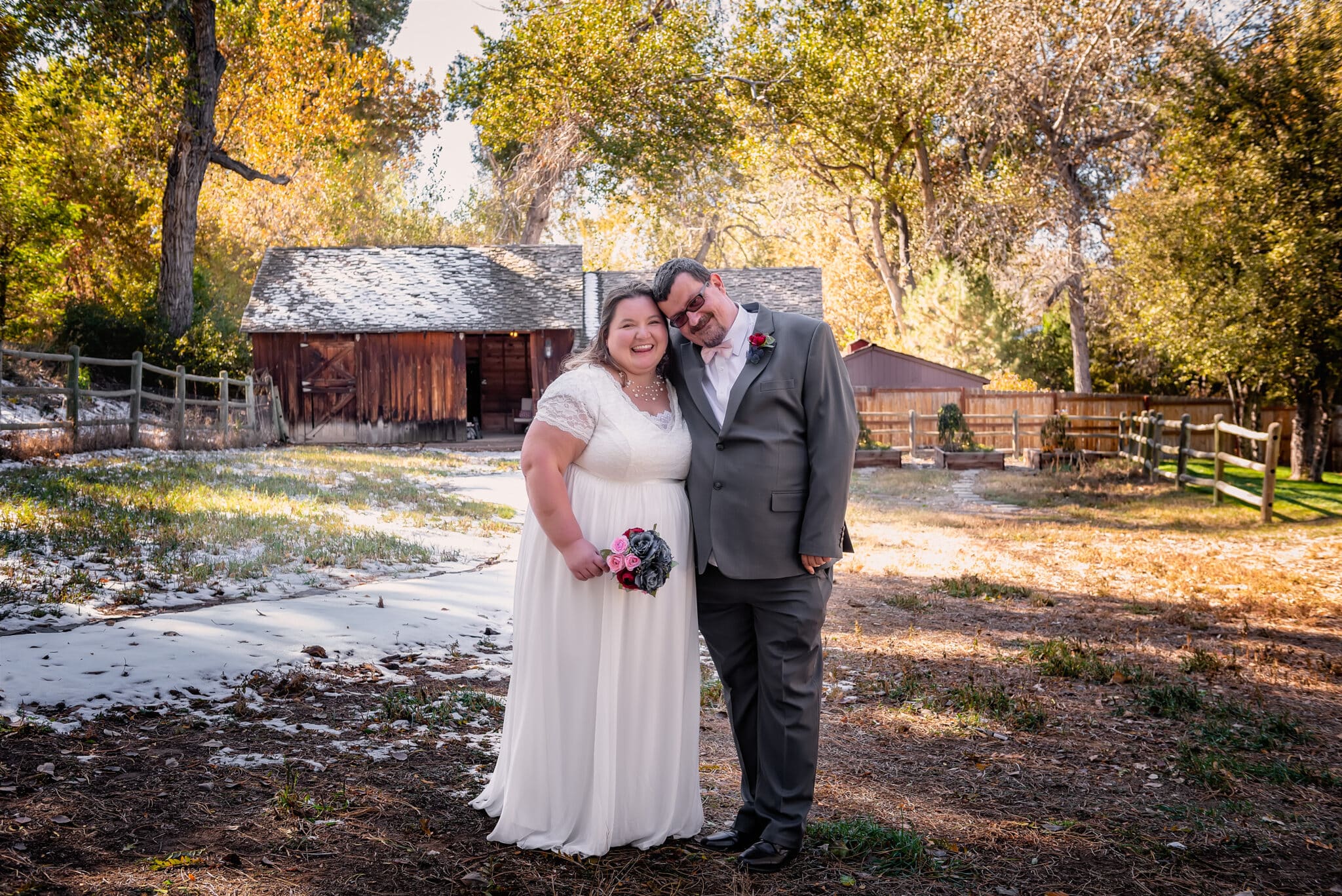 A newly married couple pose for a portrait together in the light dusting of snow amid golden leaves in front of Boyko Barn, Greenwood, Colorado.