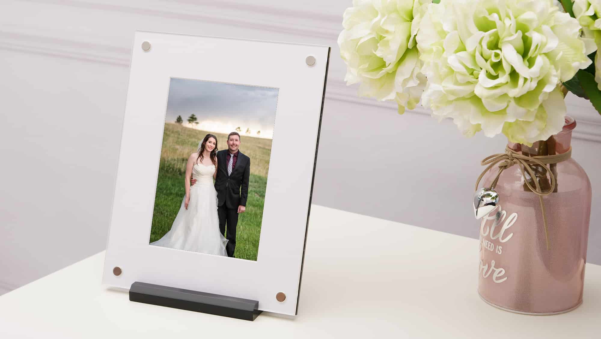 A folio style art frame that uses magnets and stands in a holder on a desk with flowers.