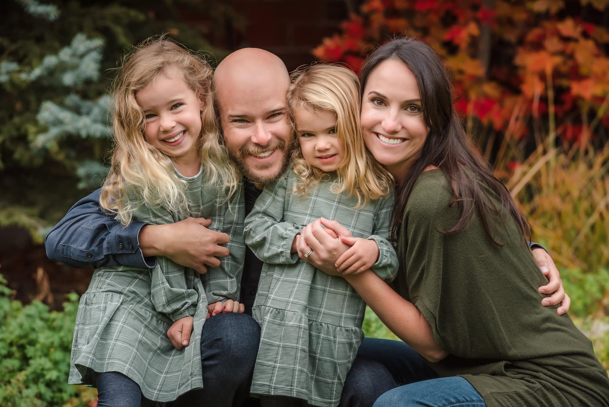 A family of four dressed in green with pretty red autumn foliage in the background.