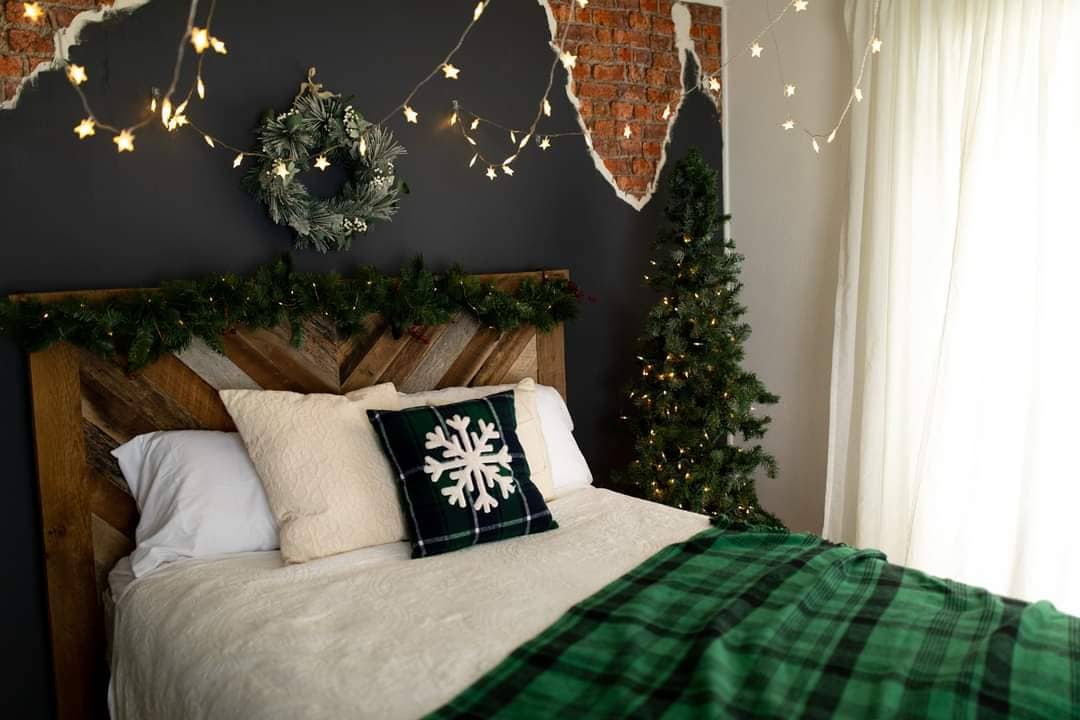 A bed decorated with a cream colored bedspread and decorated with a holiday pillow with a snowflake and a coordinating deep green check throw blanket at Studio Avenue, Loveland.