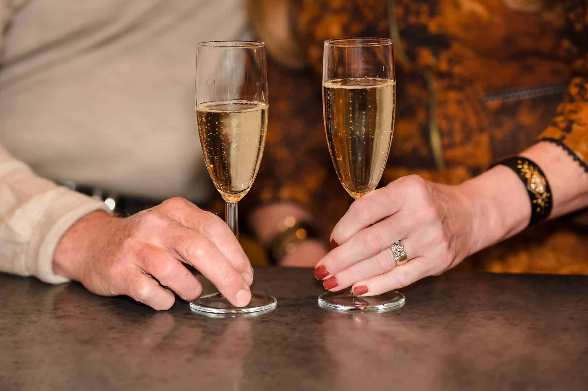 Close up of a man and woman's hands holding onto the stems of their sparkling wine.