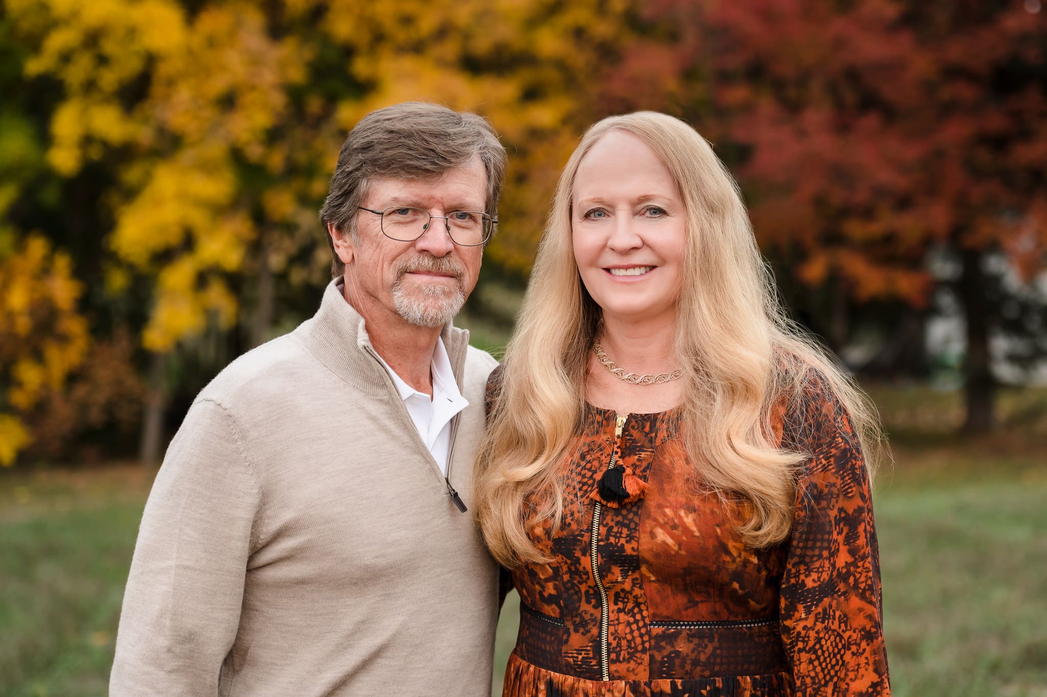 A man and woman celebrating their 40th anniversary have their photos taken in front of trees with gold and red leaves.