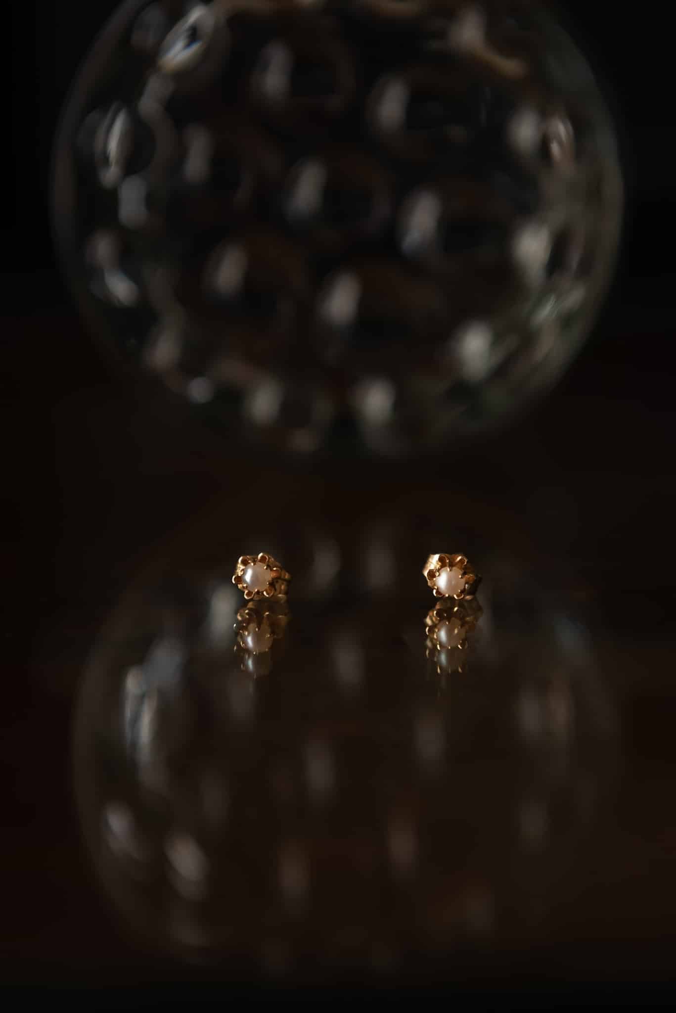 A bride's pearl earrings on a black reflective surface.