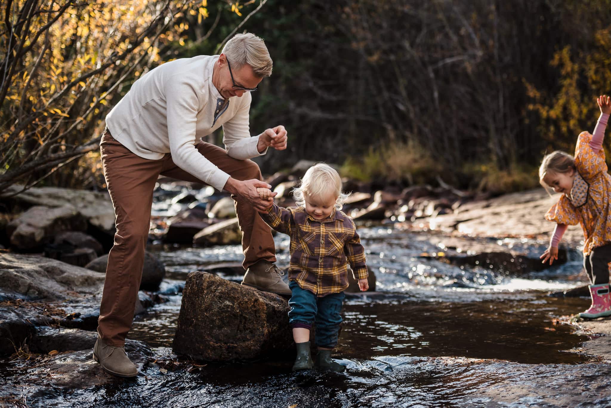 A father helps his sun over the rocks in the creek during an outdoor family portrait session.