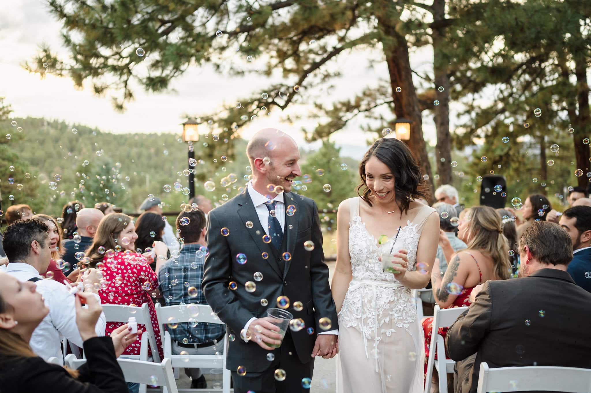 A man and woman in wedding attire dodge bubbles created by their guests during their ceremony exit.