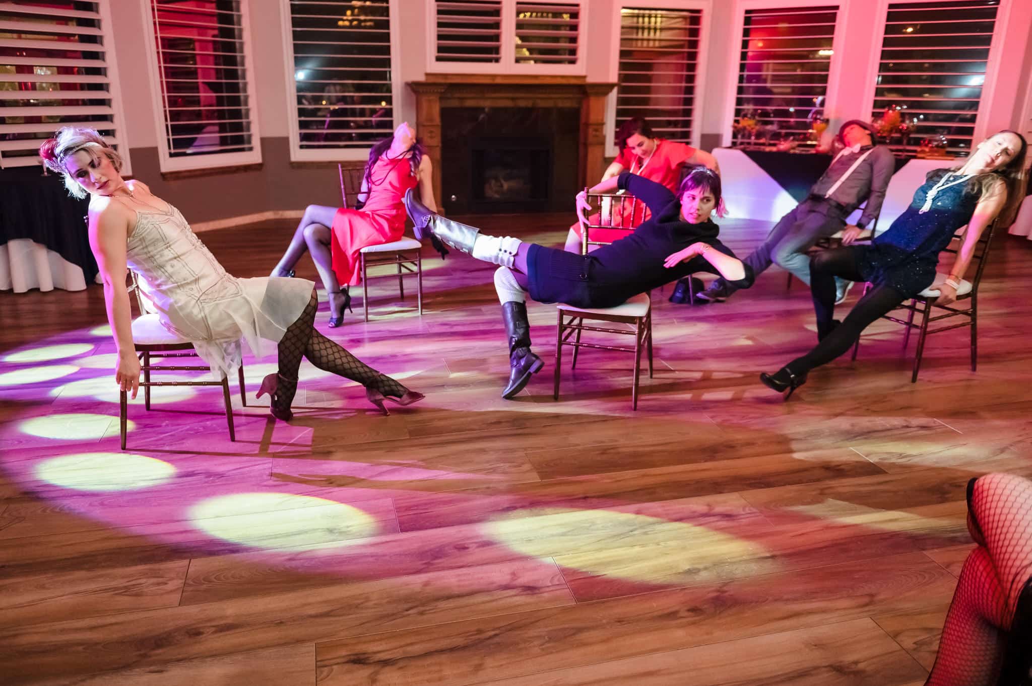 Several guests perform a dance routine they discovered on the internet that involve posing on and lifting chairs among the spotlights on the floor.
