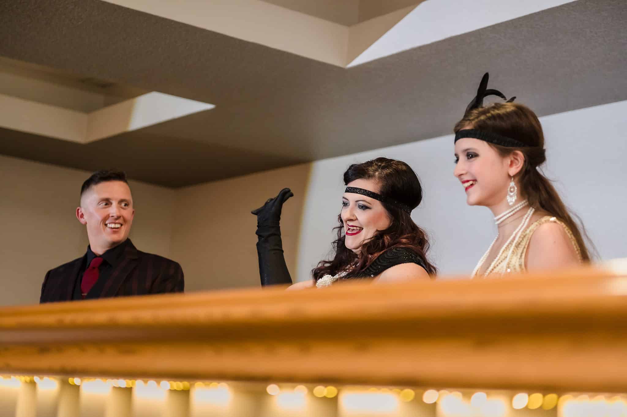 A woman waves from the balcony at her surprise 40th birthday party as her husband and teenage stepdaughter look on.