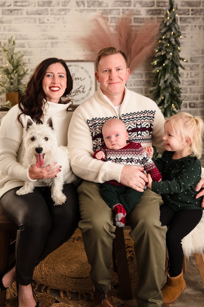 A mom, dad, baby boy, and his young sister, sit together with their puppy during a family photo session.