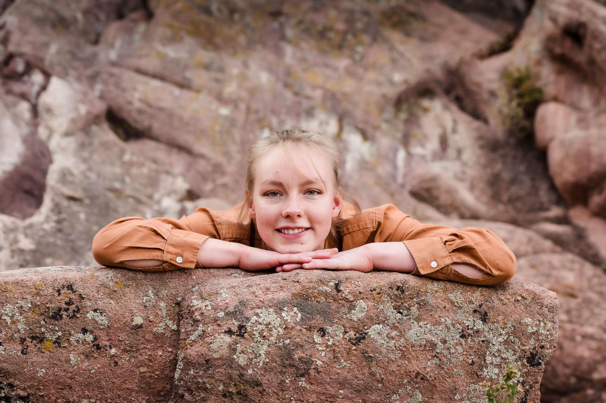 A young woman during a senior portrait session lays on a rock and smiles.