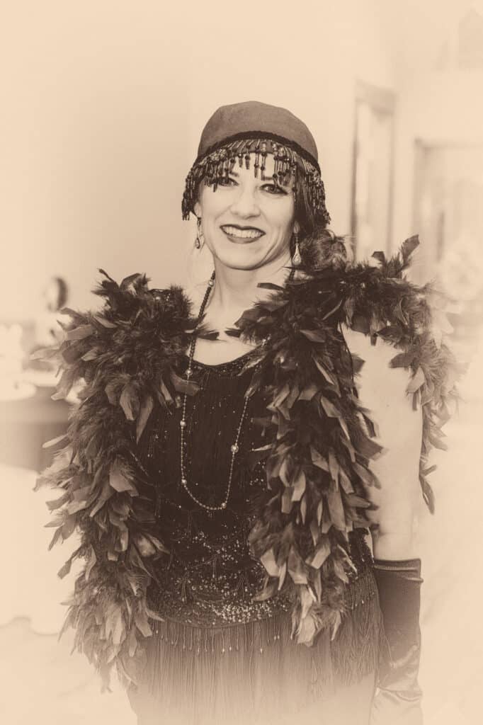 A woman dressed in 1920s attire complete with beaded headcap, feather boa, long necklace and gloves at a 40th surprise Great-Gatsby themed birthday party.