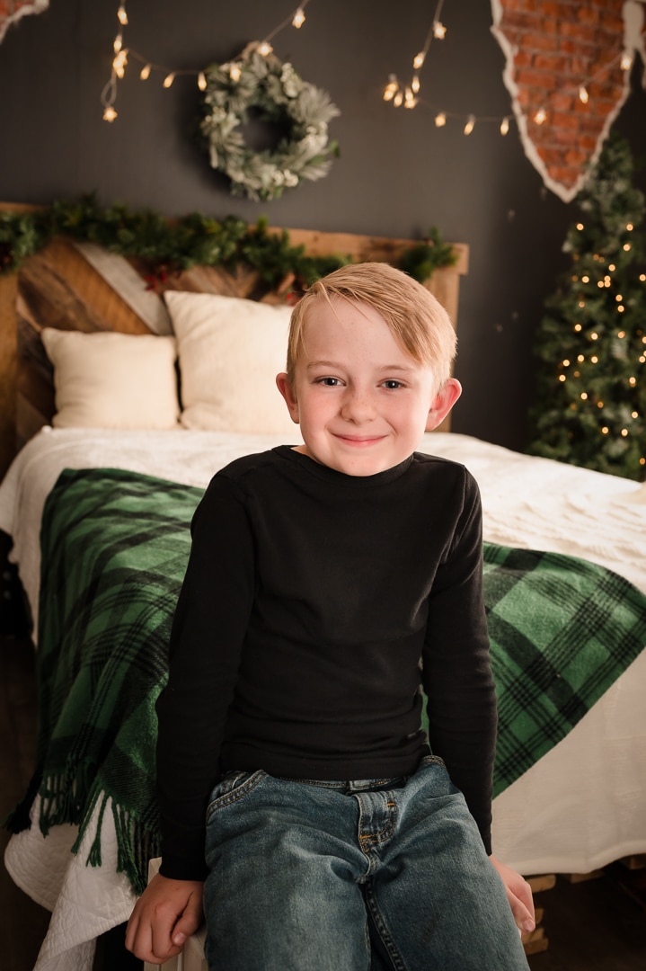 A young boy sits on the edge of a bed during the holiday photo mini session.